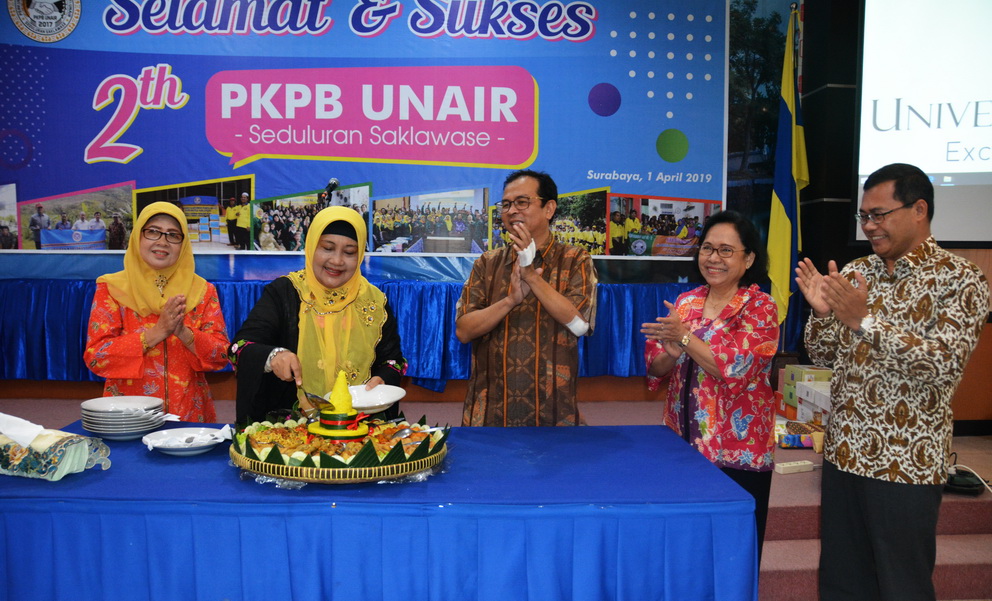 Head of PKPB UNAIR Dra. Kusmawati slices the cone-shape turmeric rice for 2nd anniversary celebration and gives the first slice to Vice Rector II Dr. Muh Madyan (third from the right) accompanied by Rosmelyani (far left, former Head of BAPSI), Sunarti (former Head of BAUK) and UNAIR HR Director Dr. Purnawan Basundoro.